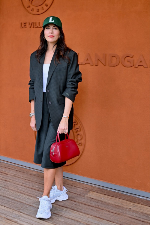 Nolwenn Leroy in full-length outfit featuring dark tailored suit, white sneakers and red handbag at Roland Garros 2025