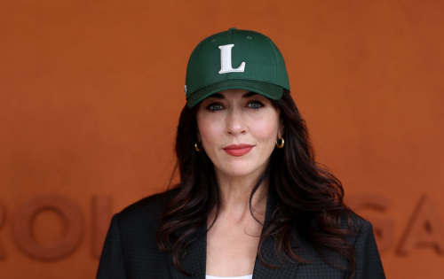 Close-up portrait of Nolwenn Leroy with subtle makeup and green Lacoste cap against Roland Garros terracotta wall at 2025 French Open
