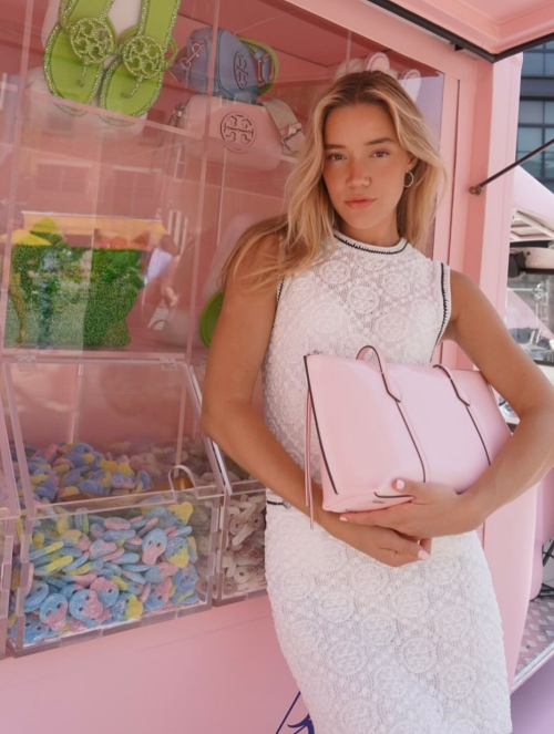 Olivia Ponton holding pink Tory Burch handbag while standing beside candy display in white lace halter dress for BonBon Collection Summer 2025