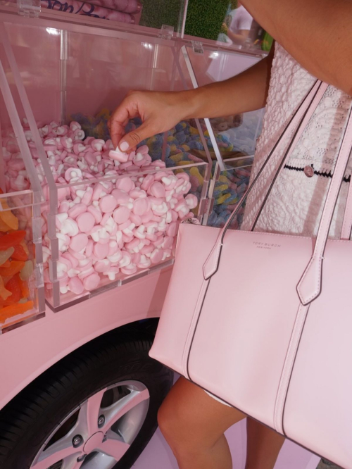 Close-up of hand selecting pink candies from display case while showcasing Tory Burch pink handbag in BonBon Collection Summer 2025 campaign