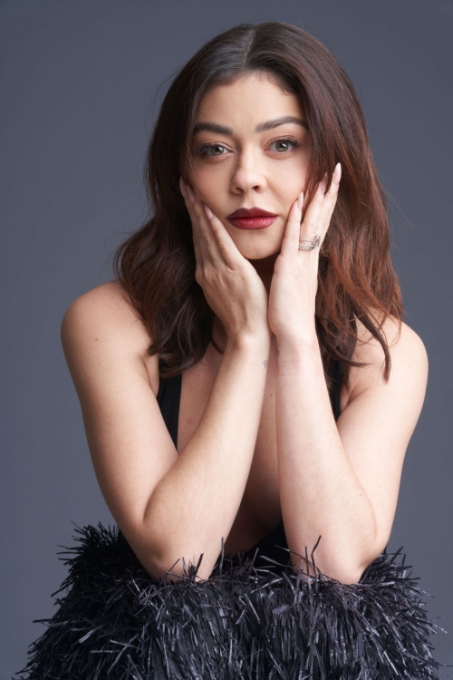 Close-up portrait of Sarah Hyland with wavy brunette bob hairstyle and red lipstick resting hands on black feathered garment for Paper Magazine June 2025 fashion spread