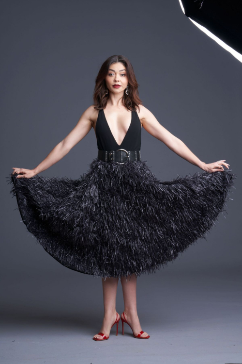 Sarah Hyland posing in black plunging neckline dress with feathered skirt, statement belt and red heels against gray backdrop for Paper Magazine June 2025 cover story