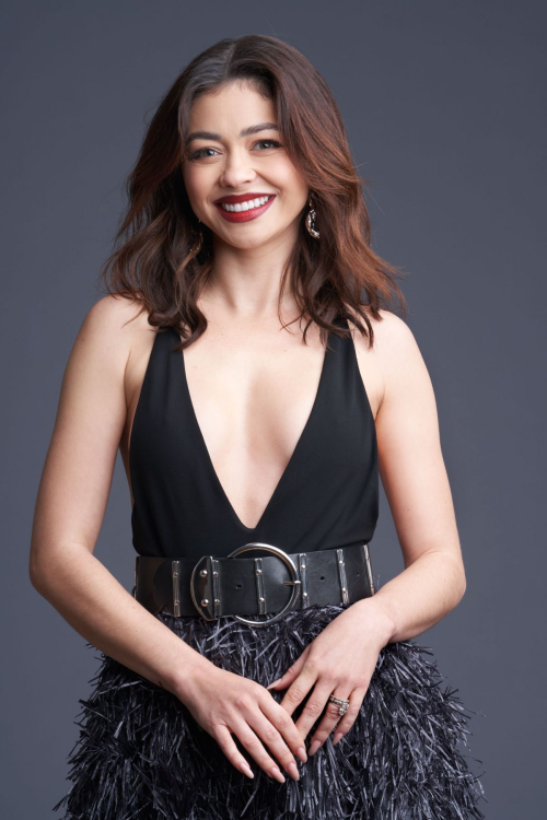 Smiling portrait of Sarah Hyland with wavy shoulder-length hair wearing black deep-V dress with feathered skirt and wide belt for Paper Magazine June 2025 feature