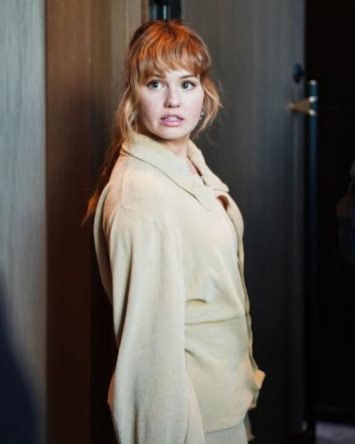 Dakota Fanning in light blue button-up shirt and beige trousers.