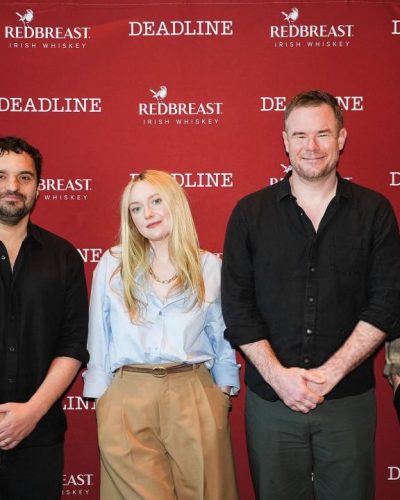 Dakota Fanning in casual light blue shirt and tailored beige trousers.