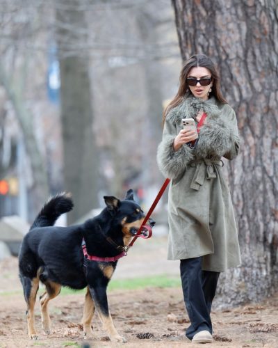 Emily Ratajkowski green coat and black trousers with casual slip-on shoes.