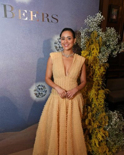 Nathalie Emmanuel wearing a nude flowing gown against diamond backdrop.