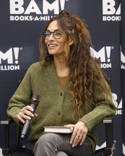 Sarah Shahi wearing a textured green cardigan and gray pants.