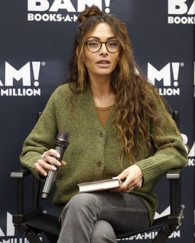 Sarah Shahi in a plush green cardigan and gray trousers.
