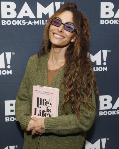 Sarah Shahi in a casual green cardigan with relaxed gray trousers.