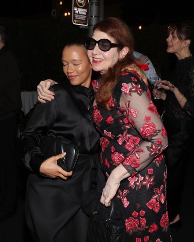 Taylor Russell in black satin shirt tucked into flowy trousers.