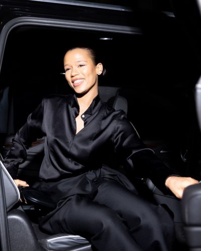 Taylor Russell wearing sleek black high-waisted pants and satin shirt.