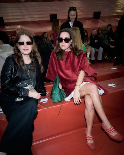 Aubrey Plaza in white pleated skirt with red poncho.