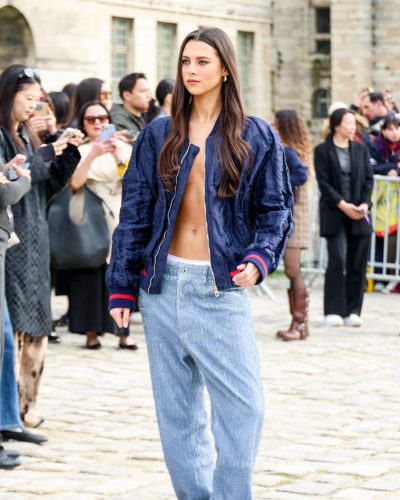 Beau Gadsdon in navy bomber jacket, light blue skirt, and hoop earrings.