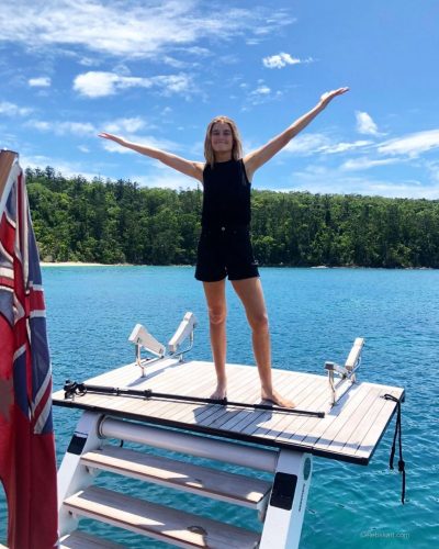Bridget Malcolm with tousled hair in black bikini by the water.
