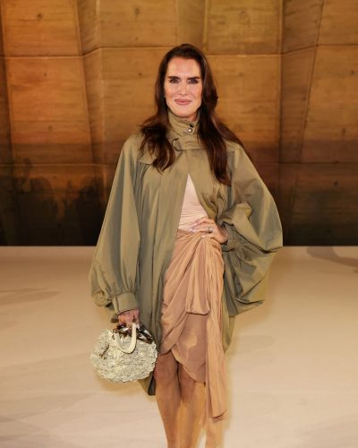 Brooke Shields in tan dress layered with olive green oversized cape.
