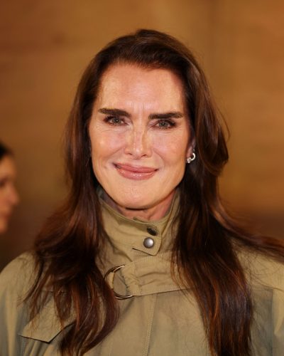 Brooke Shields in light tan dress complemented by olive green cape.