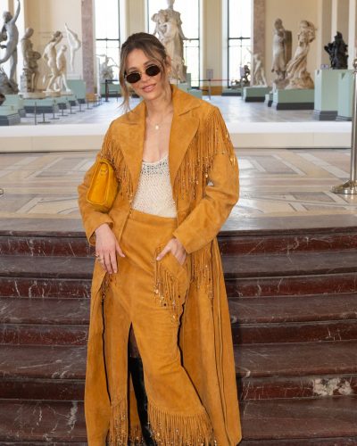 Carla Pereyra in mustard fringed coat against marble backdrop