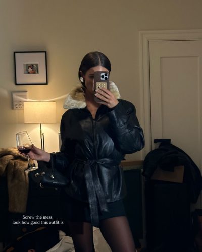 Carmella Rose in sleek black swimsuit by the water.