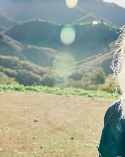 Charlize Theron in black biker jacket, white top, and tailored trousers.