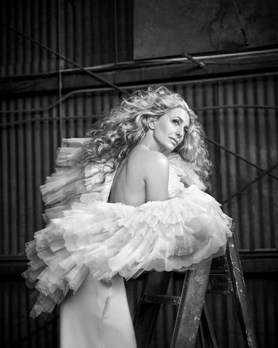 Claudia Black wearing high-waisted cream trousers and beige jacket.