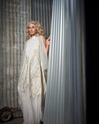 Claudia Black in chic beige jacket and cream-colored trousers.