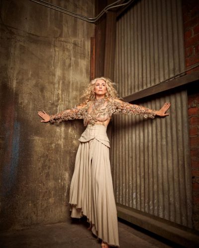 Claudia Black featuring soft curls and a beige textured jacket.