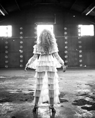 Claudia Black in high-waisted trousers paired with a beige jacket.