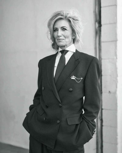 Claudia Black with cascading hair and black tailored suit.