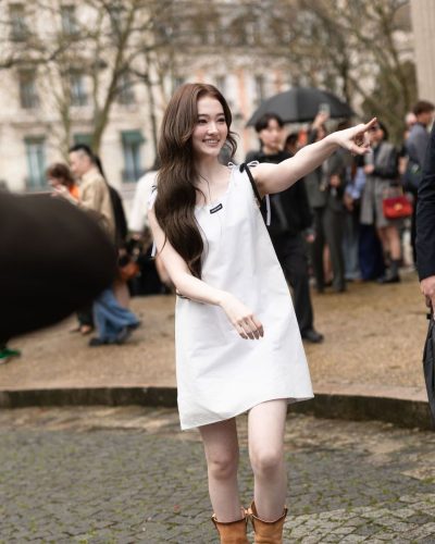 Ella Gross relaxed in white dress against floral backdrop.