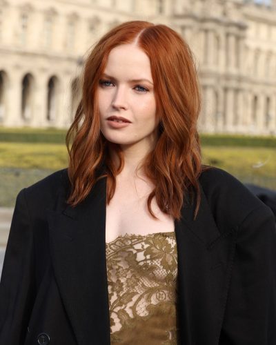 Ellie Bamber styled in black oversized coat over olive green lace dress.