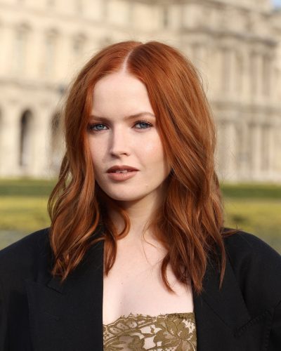 Ellie Bamber in black oversized coat layered over olive green dress.