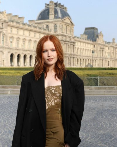 Ellie Bamber in sophisticated olive green lace dress and black coat.