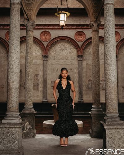 Halle Bailey in a modern one-shoulder white dress and hoop earrings.