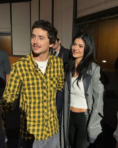 Timothée Chalamet in yellow checkered shirt and grey trousers.