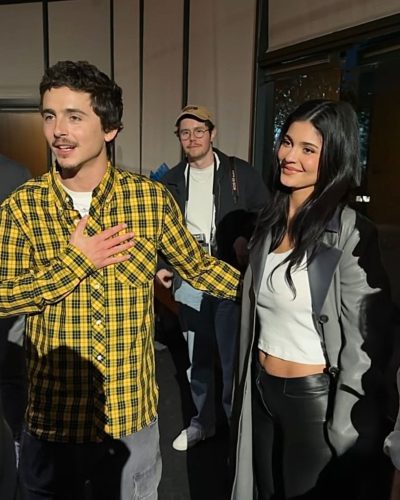 Timothée Chalamet sporting playful yellow checkered shirt and grey pants.