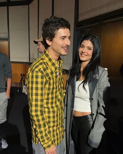 Timothée Chalamet in vibrant yellow shirt and casual grey trousers.