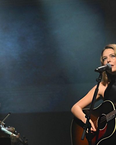 Maggie Rogers in black dress complemented by warm spotlight.