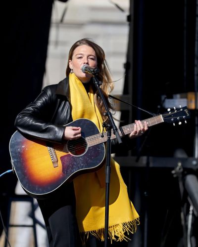 Maggie Rogers bold black leather jacket and cheerful yellow scarf