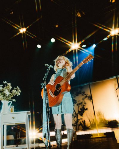 Maisie Peters in a soft pastel dress and bold black knee-high boots.