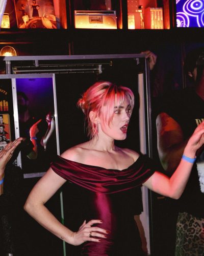 Meg Donnelly sporting a lively deep red gown with bold makeup.