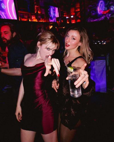 Meg Donnelly in a deep red gown reflecting vibrant lights.