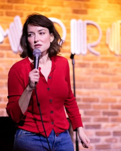 Milana Vayntrub in relaxed fit blue jeans and red cardigan.