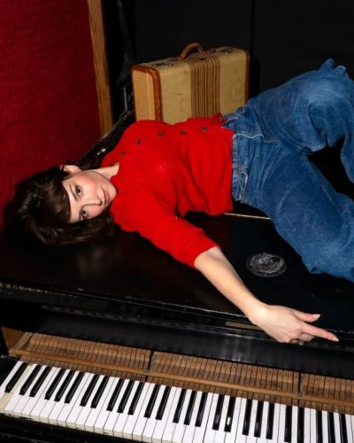 Milana Vayntrub styled in a button-up red cardigan and jeans.