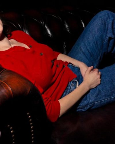Milana Vayntrub styled in a red cardigan and high-waisted jeans.