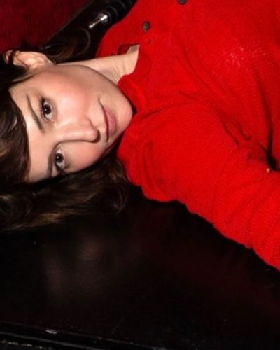 Milana Vayntrub in casual blue jeans and vibrant red cardigan.