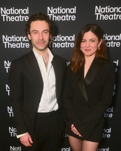 Monica Barbaro with a black blazer and delicate gold earrings.