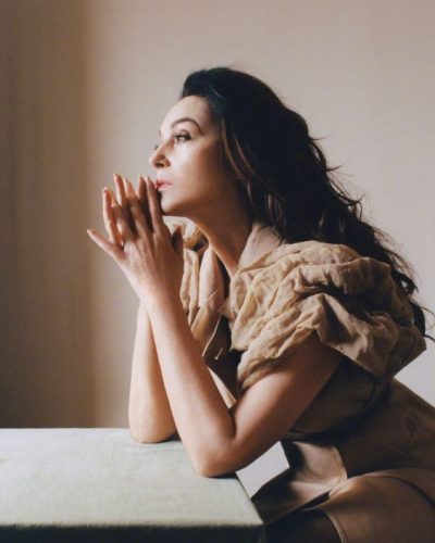 Monica Bellucci wearing a minimalist beige dress with bold sleeves.