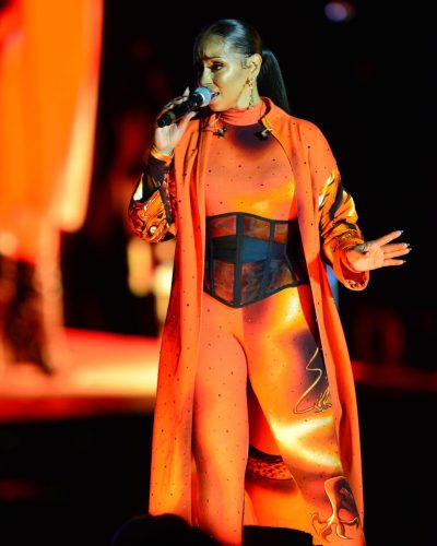 Mya wearing fitted orange bodysuit with flowing graphic coat