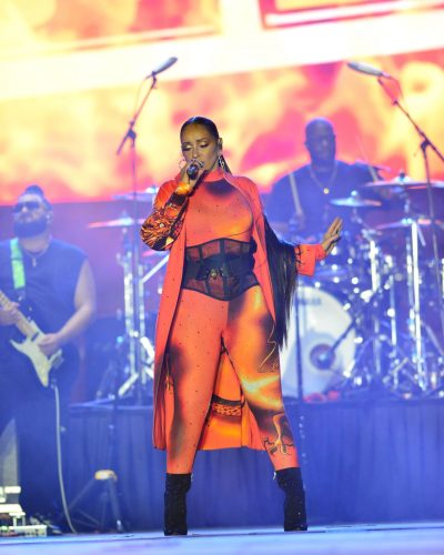 Mya in colorful orange bodysuit with dramatic coat